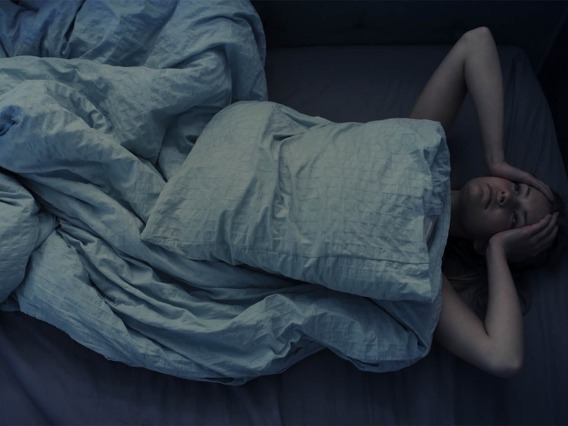 woman lying in bed with hands on head in frustration unable to sleep