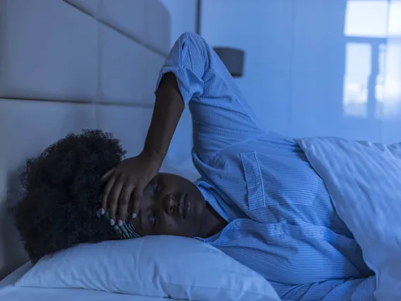 a woman lying in bed in a dark room unable to sleep with her hand on her forehead