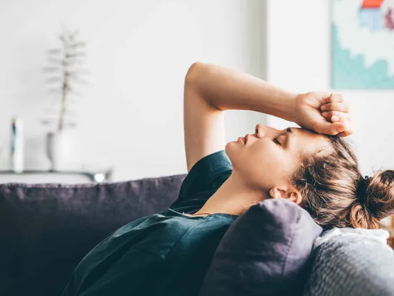 person laying on couch with hand on forehead