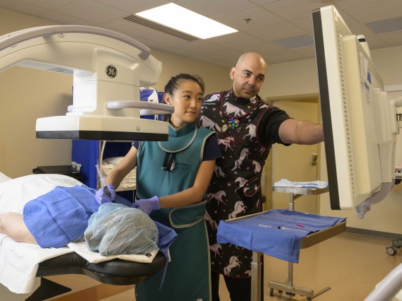 Two pain management doctors view x-rays on a screen while conducting a procedure on a patient