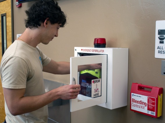 student placing naloxone kit into an automated external defibrillator cabinet