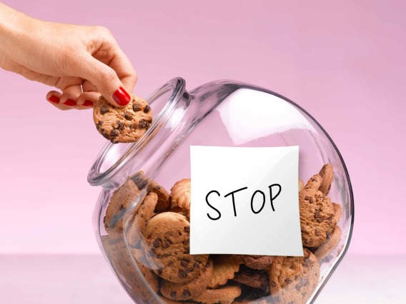 Hand taking a chocolate chip cookie from a cookie jar that has a hand-written note that says “STOP” on the side