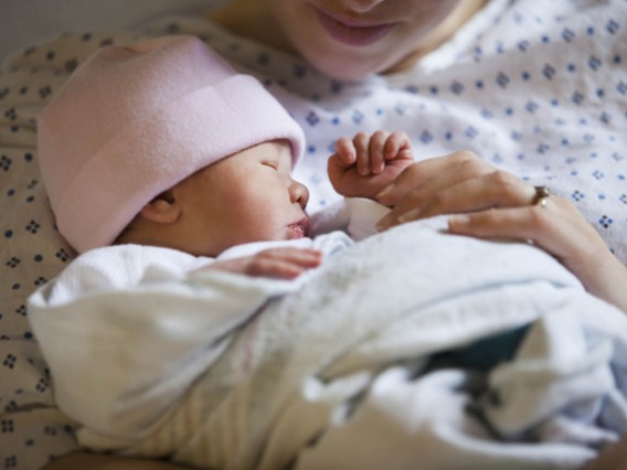 close up of infant in pink cap held by person in hospital gown