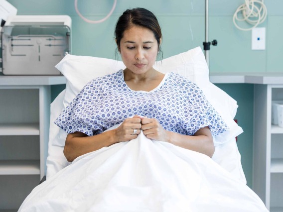 person laying in hospital bed, looking down, hands clenching blanket