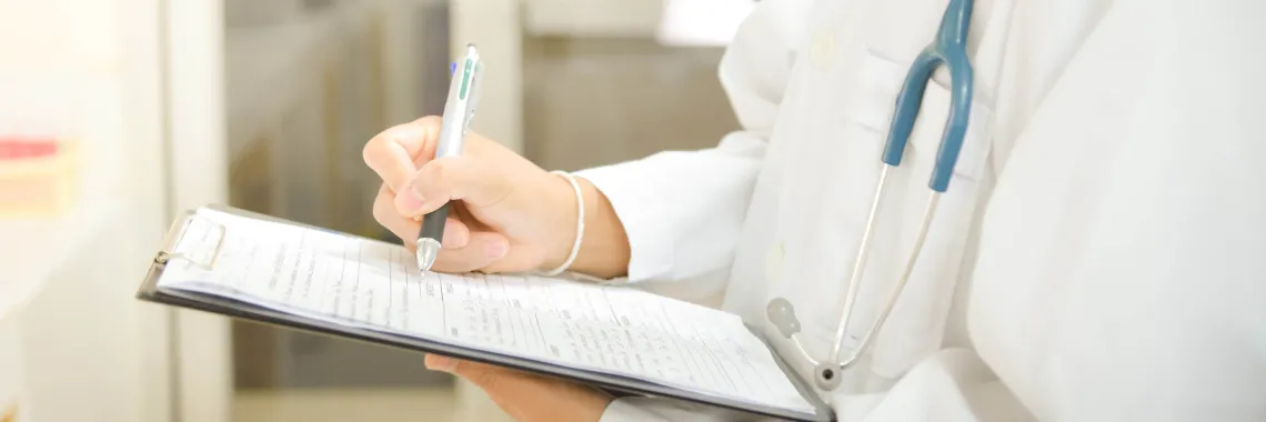 closeup of doctor writing on clipboard with stethoscope around neck