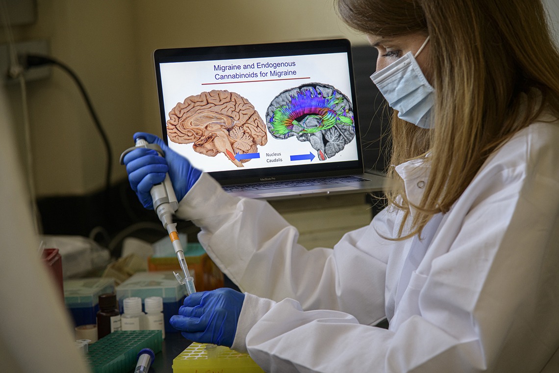 researcher using a pipette in front of a computer monitor displaying illustrated image of brain