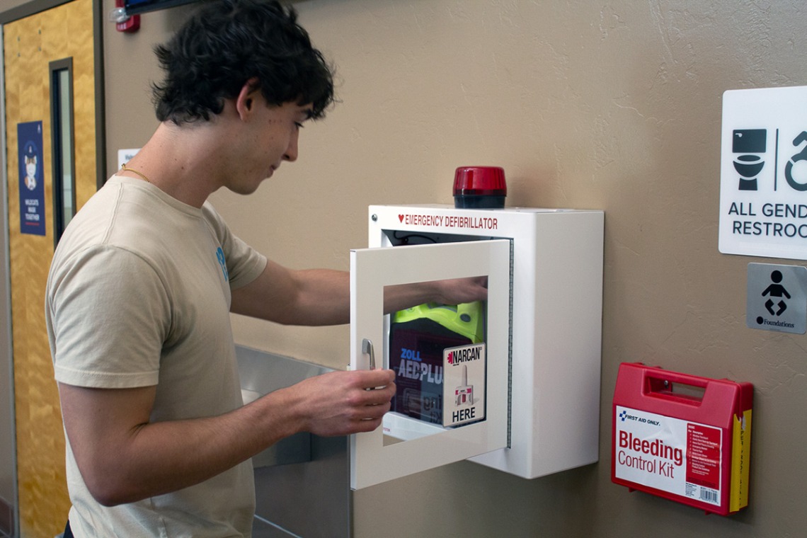 student placing naloxone kit into an automated external defibrillator cabinet