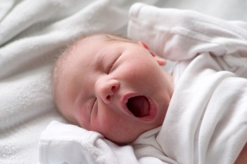 baby on white blanket yawning