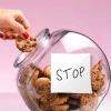 Hand taking a chocolate chip cookie from a cookie jar that has a hand-written note that says “STOP” on the side