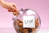 Hand taking a chocolate chip cookie from a cookie jar that has a hand-written note that says “STOP” on the side